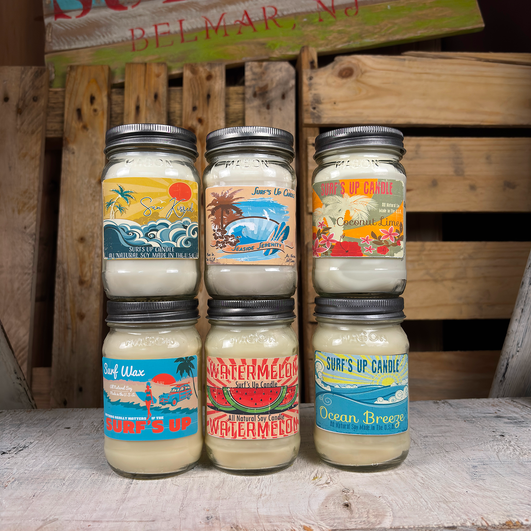 Six jars of candles with colorful labels on a wooden surface.