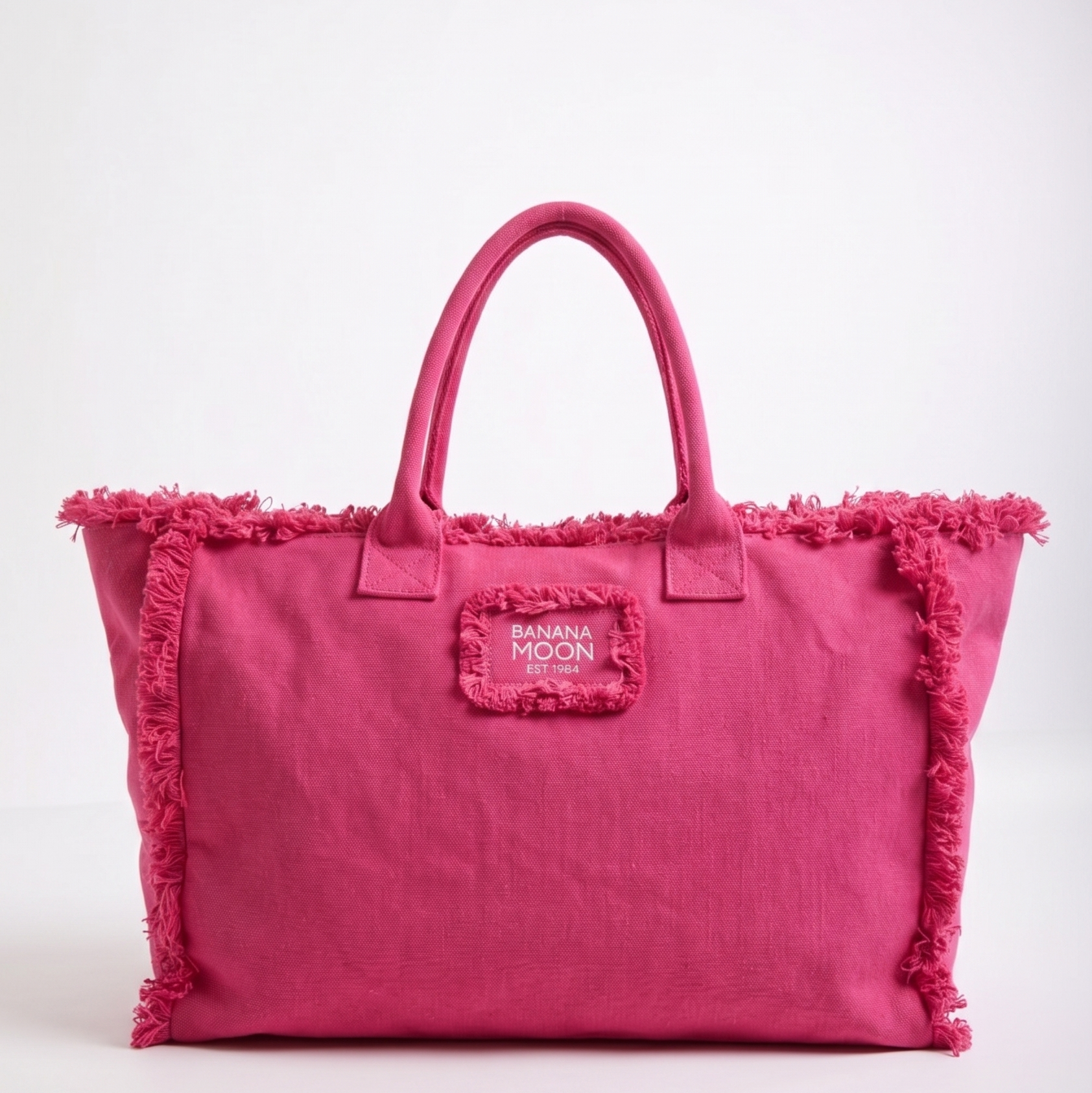 Pink tote bag with fringe details and a visible brand logo on a white background